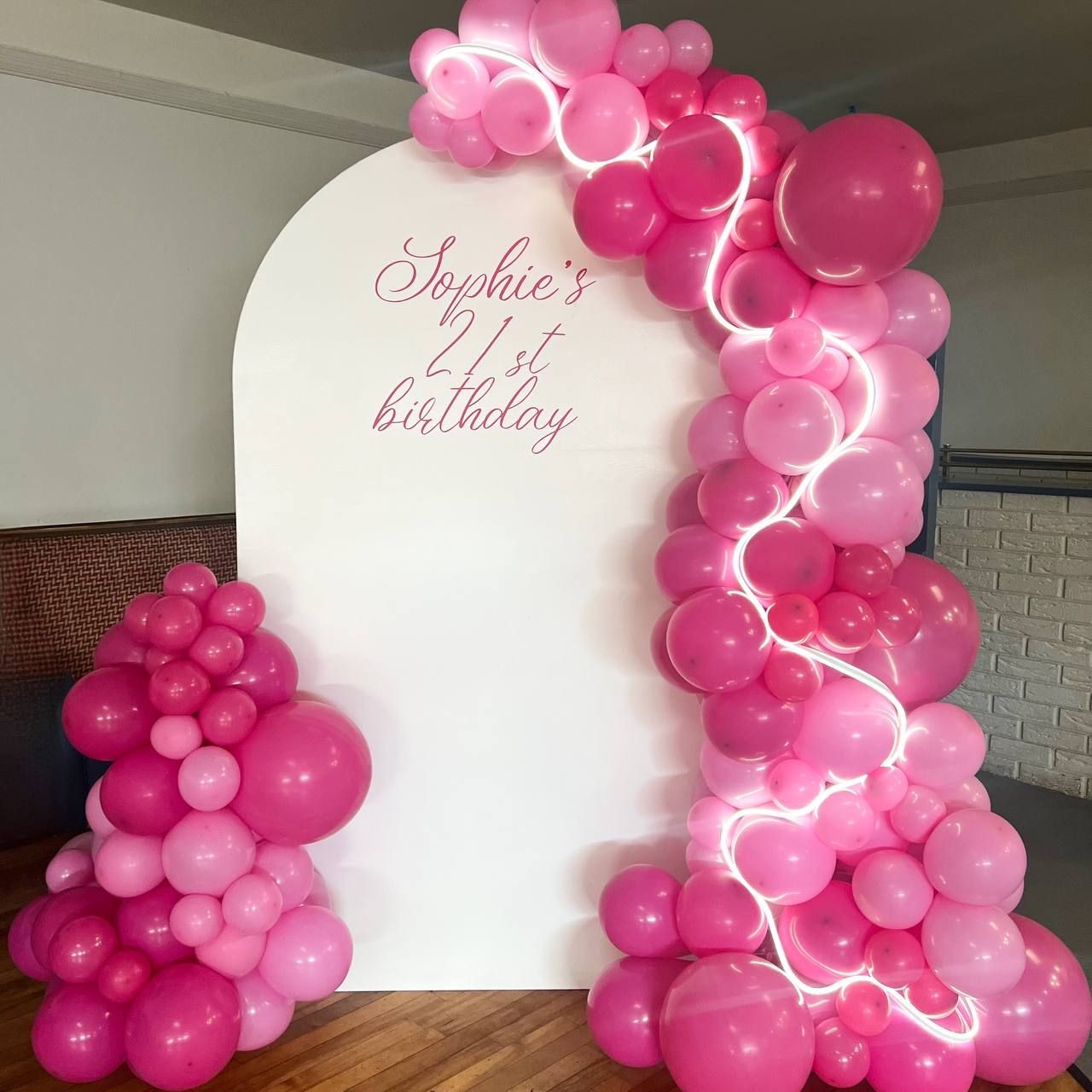 Pink balloon arch with 'Sophie's 21st birthday' sign on white background.