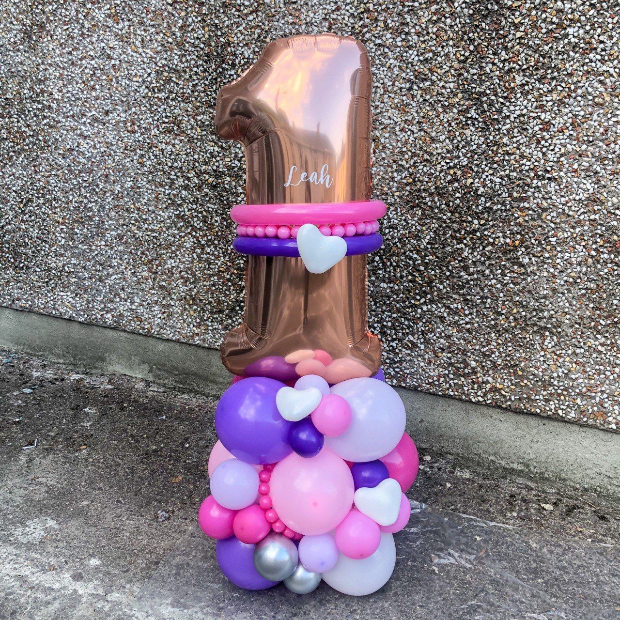 Tall balloon arrangement for a first birthday with metallic number one and pastel colored balloons.