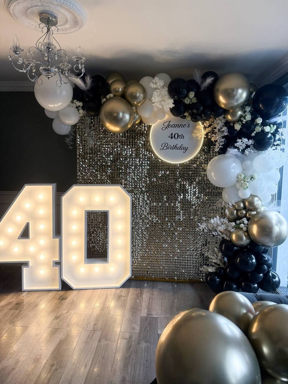 Elegant 40th birthday decor with balloons, sequin backdrop, and illuminated number 40.
